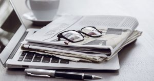 Laptop, Newspaper, Spectacles, Pen and Coffee cup placed on white table