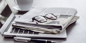 Laptop, Newspaper, Spectacles, Pen and Coffee cup placed on white table